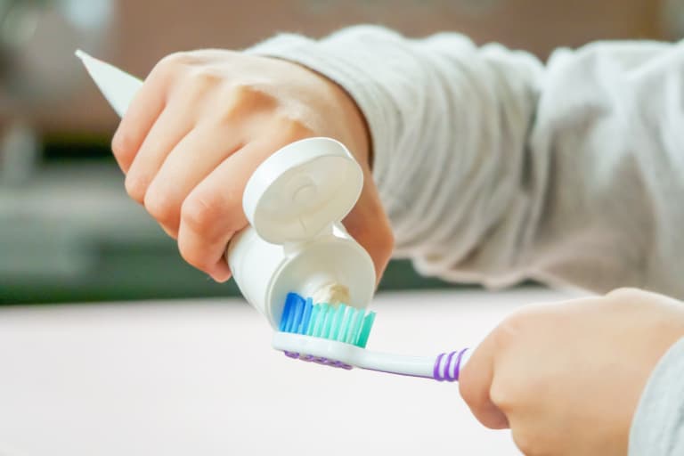 child putting toothpaste on toothbrush